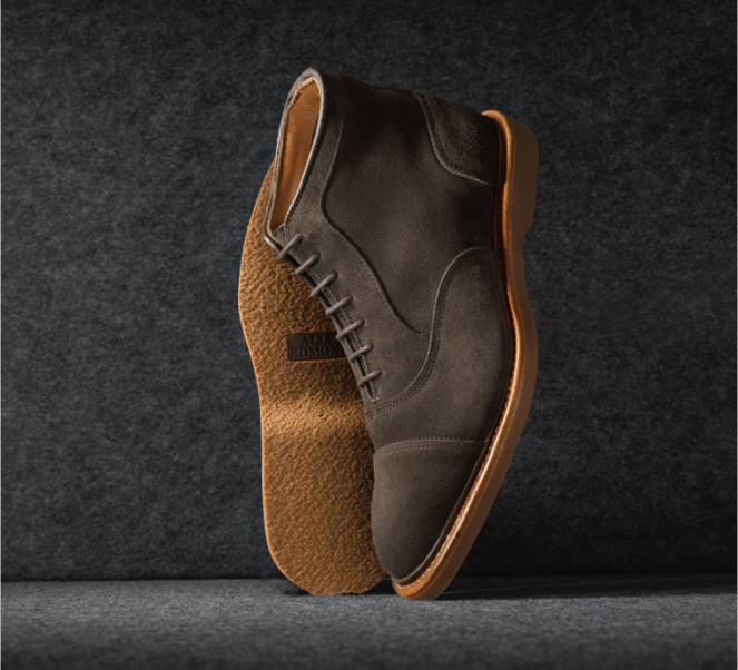 A pair of brown suede cap-toe oxford boots displayed vertically, with one sole facing forward.  