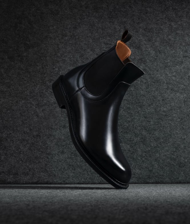 One black leather Chelsea boot displayed vertically with the toe facing downward.  