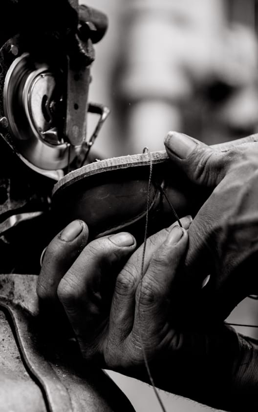 A pair of hands holding a men’s dress shoe up to a machine that attaches the sole to the upper.  