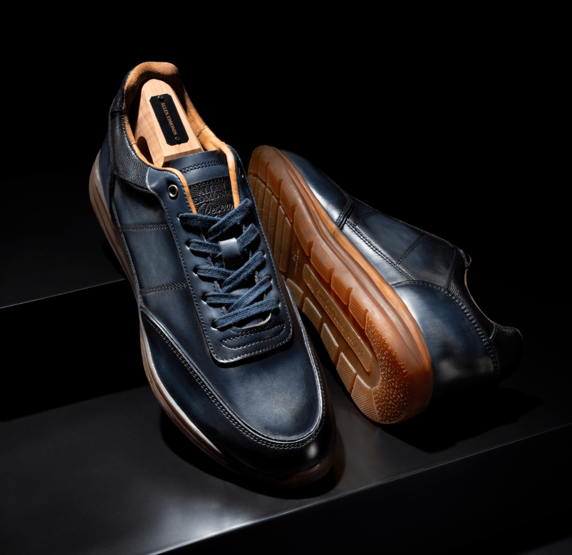 Close up of navy leather Allen Edmonds Brentwood sneakers displayed with a branded cedar shoe tree and showcasing the textured gum sole