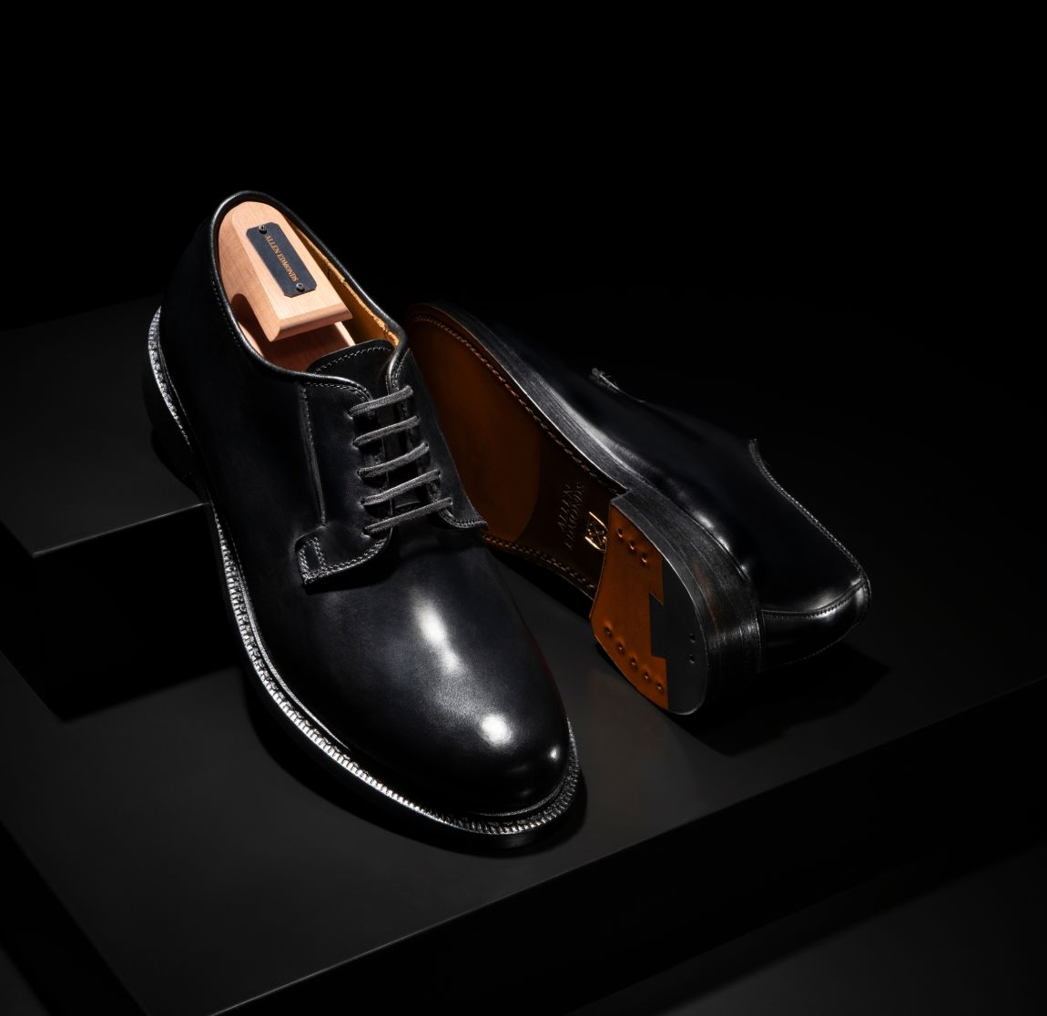 Black leather Allen Edmonds Rowan derby dress shoes displayed with a branded cedar shoe tree against a dark background 